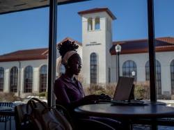 Woman sitting at a table with a laptop in front of window.